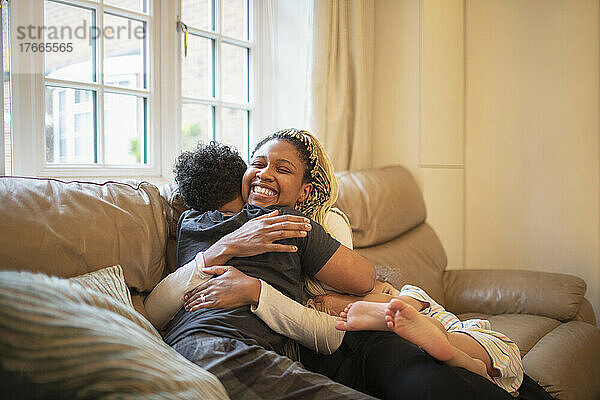 Glückliche Mutter und Sohn umarmen sich auf dem Sofa im Wohnzimmer
