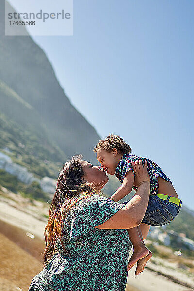 Glückliche  liebevolle Mutter küsst Sohn am sonnigen Strand