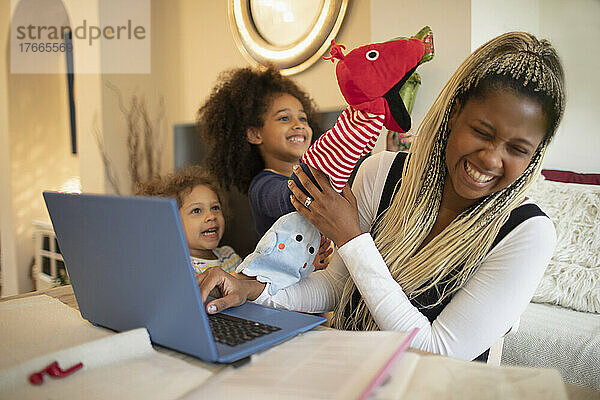 Verspielte Töchter mit Puppen lenken Mutter bei der Arbeit am Laptop ab