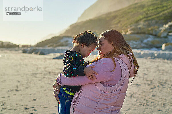 Zärtliche Mutter hält Sohn mit Down-Syndrom am sonnigen Strand