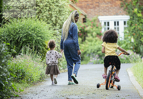 Mutter und Töchter gehen in der Einfahrt spazieren und fahren Fahrrad