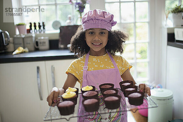 Porträt eines glücklichen süßen Mädchens  das Cupcakes auf einem Gestell backt