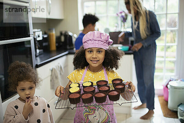 Porträt eines süßen Mädchens  das in der Küche ein Regal mit gebackenen Cupcakes hält