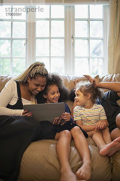 Mutter und Töchter nutzen digitales Tablet auf dem Sofa im Wohnzimmer