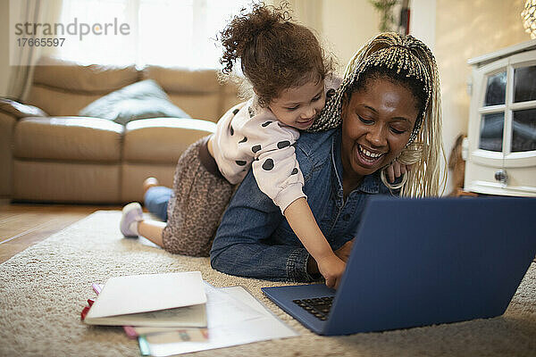 Neugierige Tochter beobachtet Mutter  wie sie am Laptop auf dem Boden arbeitet