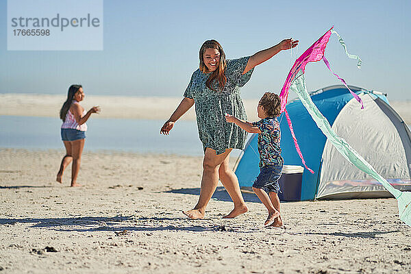 Glückliche Mutter und Sohn spielen mit Drachen am sonnigen Strand
