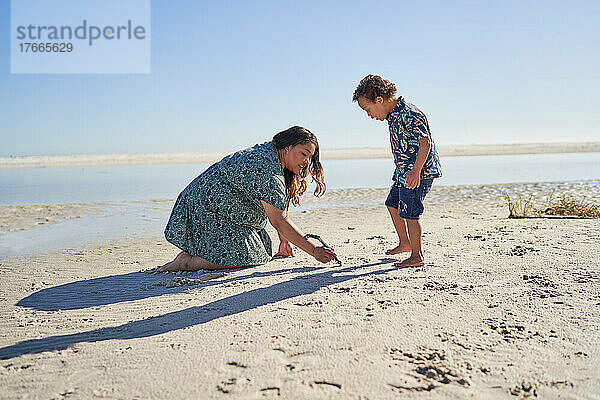Mutter und Sohn mit Down-Syndrom zeichnen mit Stock am Strand im Sand