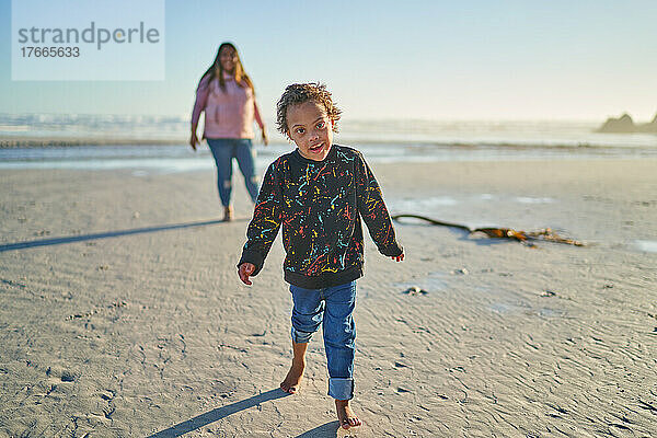 Porträt eines süßen Jungen mit Down-Syndrom  der am sonnigen Strand spaziert