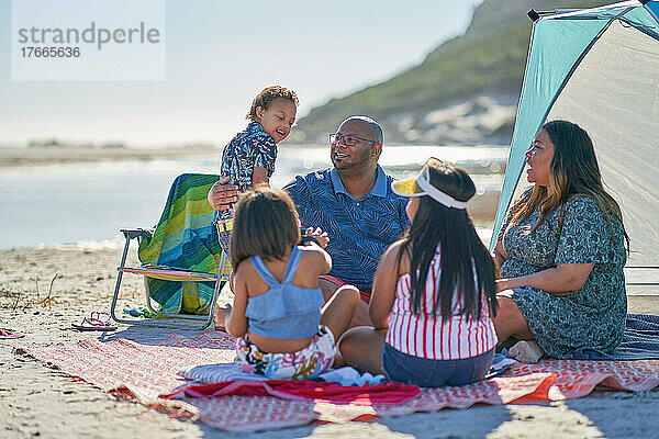 Glückliche Familie sitzt auf einer Decke am sonnigen Sommerstrand