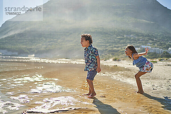 Bruder und Schwester spielen in der sonnigen Meeresbrandung am Strand
