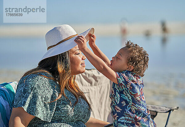 Neugieriger Sohn mit Down-Syndrom hebt am Strand den Hut der Mutter