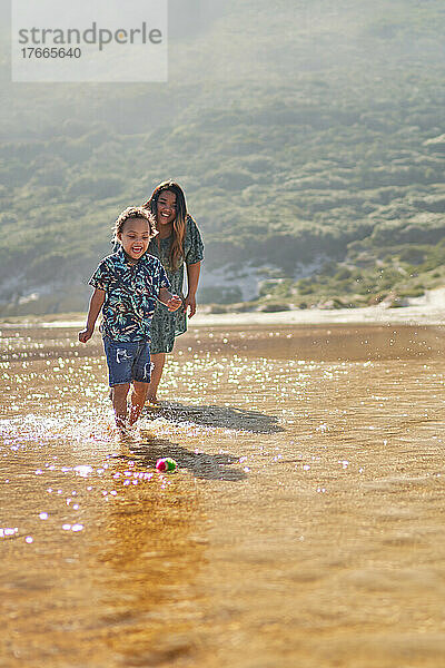Glückliche Mutter und Sohn spielen mit Ball in der Meeresbrandung