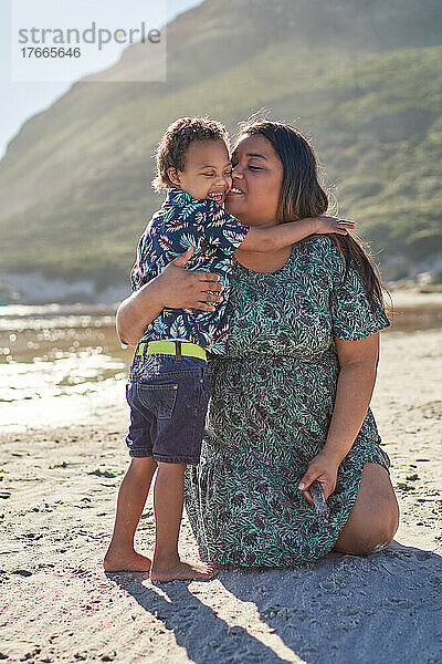 Zärtliche Mutter umarmt glücklichen Sohn am sonnigen Strand