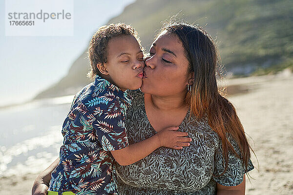Glückliche  liebevolle Mutter und Sohn küssen sich am sonnigen Strand