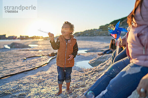 Netter Junge mit Down-Syndrom  der am sonnigen Strand mit Seifenblasen spielt
