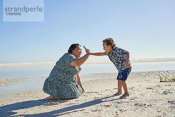 Glückliche Mutter und Sohn feiern High-Five am sonnigen Meeresstrand