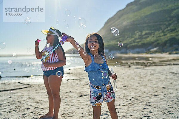 Schwestern spielen mit Seifenblasen am sonnigen Strand
