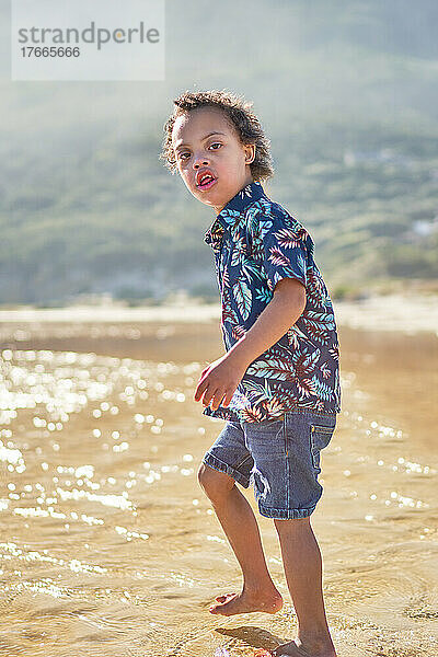 Porträt eines Jungen mit Down-Syndrom  der am sonnigen Strand im Meer watet