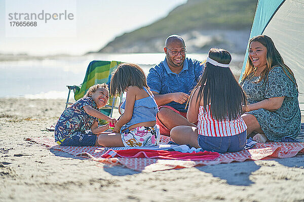 Glückliche Familie auf Picknickdecke am sonnigen Strand