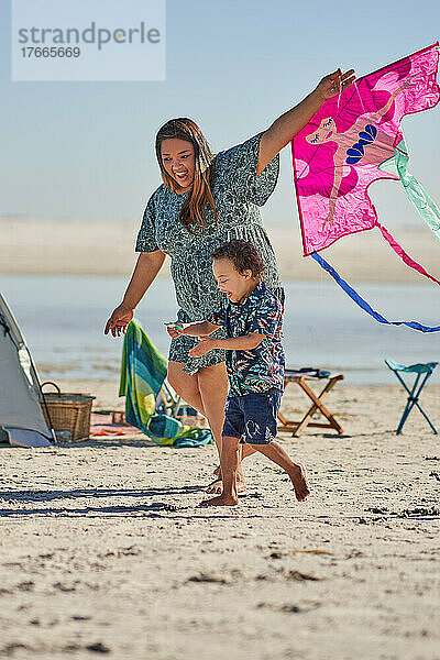 Glückliche Mutter und Sohn spielen mit Drachen am sonnigen Strand