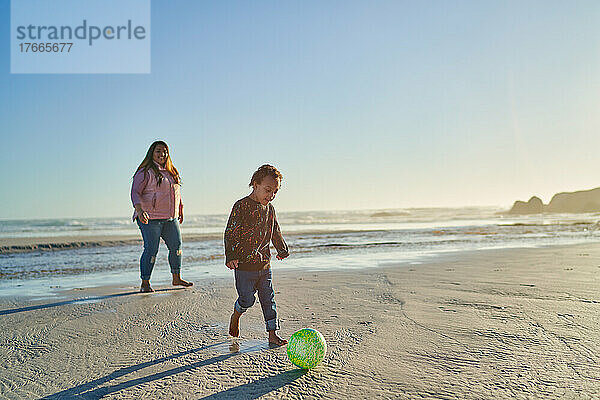 Mutter und Sohn mit Down-Syndrom spielen mit Fußball am Strand