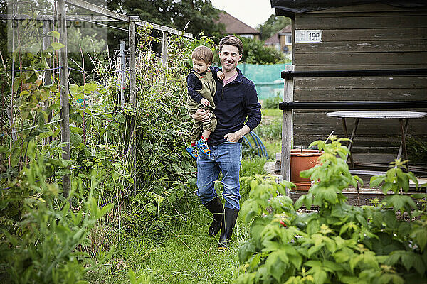 Glücklicher Vater trägt seinen kleinen Sohn im Gemüsegarten