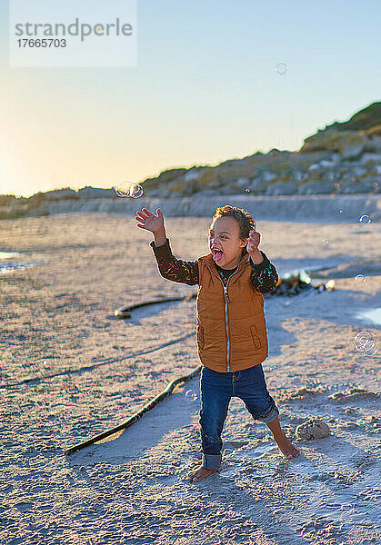 Fröhlicher  unbeschwerter Junge mit Down-Syndrom  der am Strand mit Seifenblasen spielt