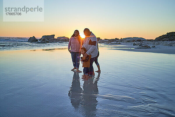 Familie watet bei Sonnenuntergang im nassen Sand am Meeresstrand