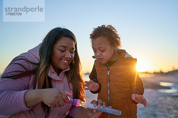 Glückliche Mutter und Sohn mit Down-Syndrom spielen mit Seifenblasen am Strand