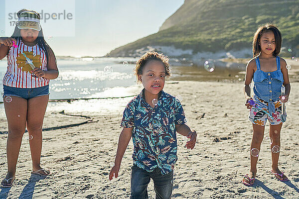 Schwestern und Bruder mit Down-Syndrom spielen mit Seifenblasen am Strand