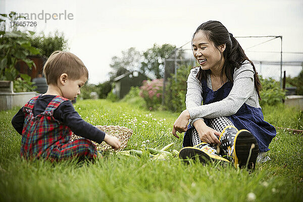 Glückliche Mutter beobachtet Sohn beim Gemüse im Gartengras