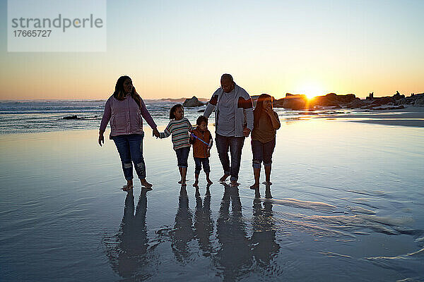 Familie hält Händchen im nassen Sand am Strand bei Sonnenuntergang