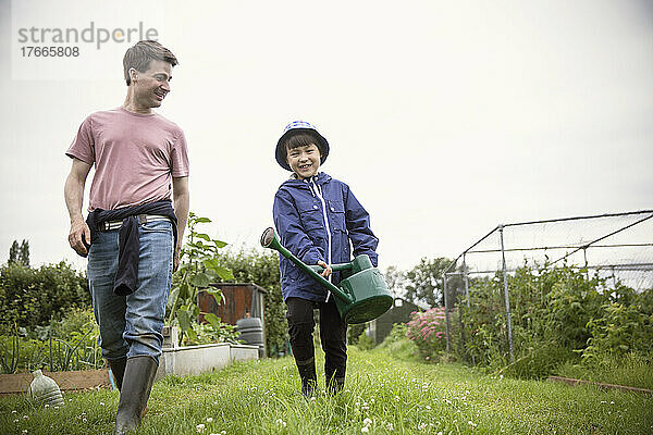 Vater und Sohn gehen mit Gießkanne im Garten spazieren
