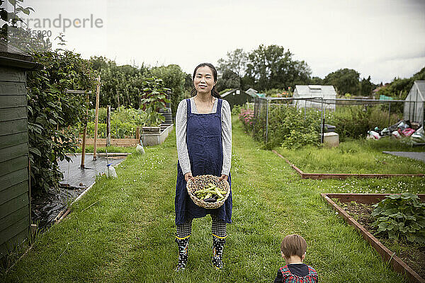 Porträt einer lächelnden Frau mit einem Korb voller Gemüse im Garten