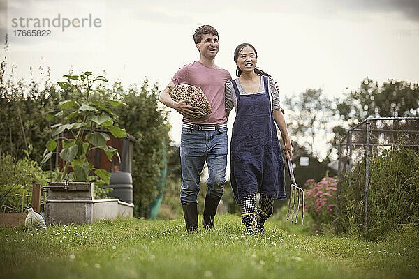 Glückliches Paar geht mit Gemüse und Heugabel im Garten spazieren
