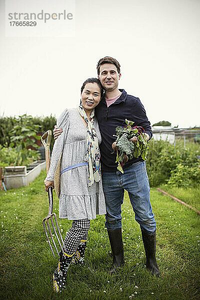 Porträt eines glücklichen Paares mit geerntetem Gemüse im Garten