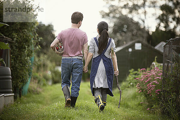 Paar geht mit Heugabel und Gemüse im Garten spazieren