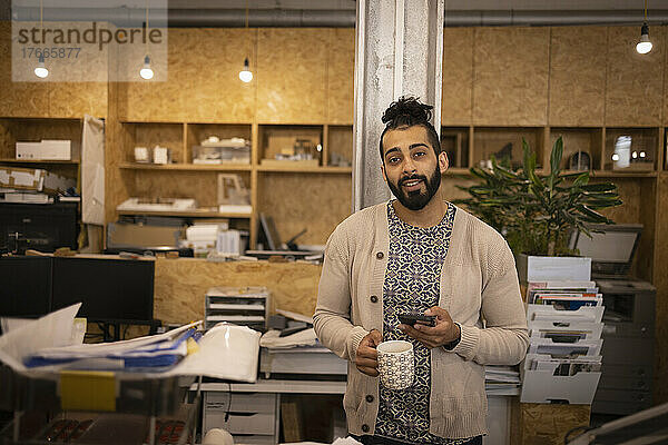 Porträt eines selbstbewussten jungen männlichen Designers mit Kaffee und Telefon