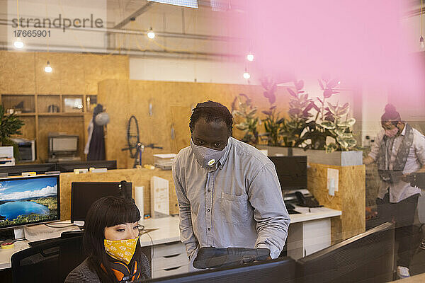 Geschäftsleute mit Gesichtsmasken unterhalten sich am Schreibtisch im Büro