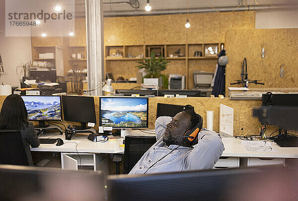 Geschäftsmann mit Headset liegt im Büro  die Hände hinter dem Kopf