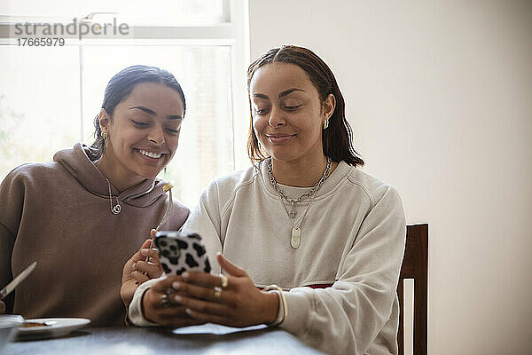Lächelnde junge erwachsene Schwestern  die zu Hause ihr Smartphone benutzen