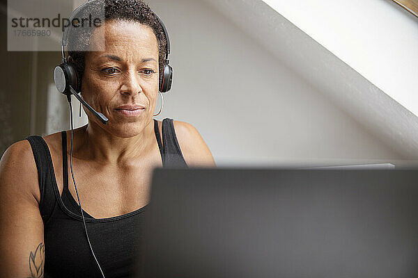 Reife Frau mit Headset arbeitet von zu Hause aus am Laptop