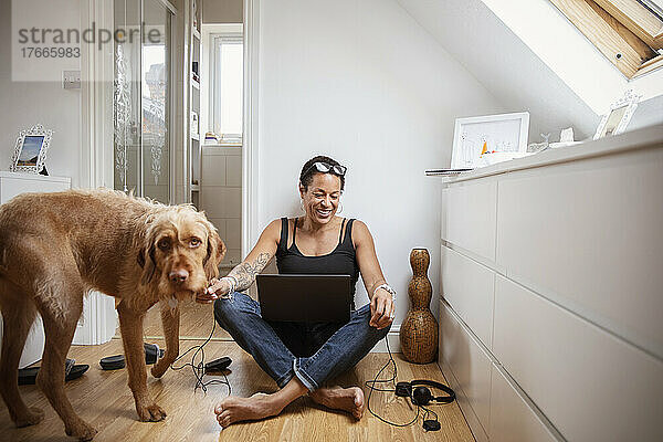 Glückliche Frau mit Hund und Laptop auf dem Schlafzimmerboden