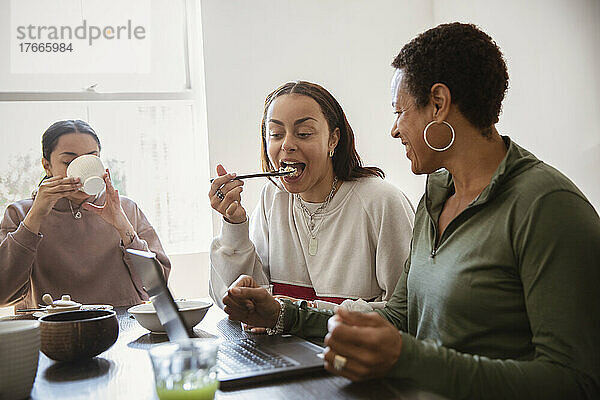 Mutter und junge erwachsene Töchter essen am Laptop
