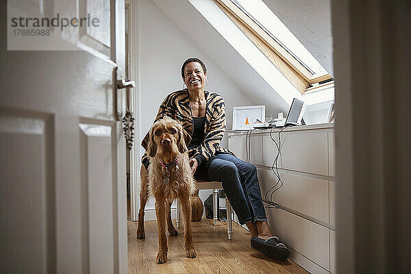 Porträt einer glücklichen Frau mit Hund im Heimbüro