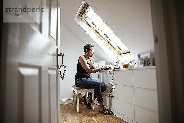 Reife Frau arbeitet von zu Hause aus am Laptop im Schlafzimmer