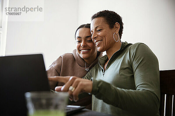 Glückliche Mutter und junge erwachsene Tochter benutzen Laptop