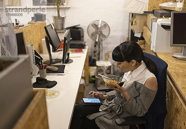 Geschäftsfrau isst Mittagessen und benutzt Smartphone im Büro