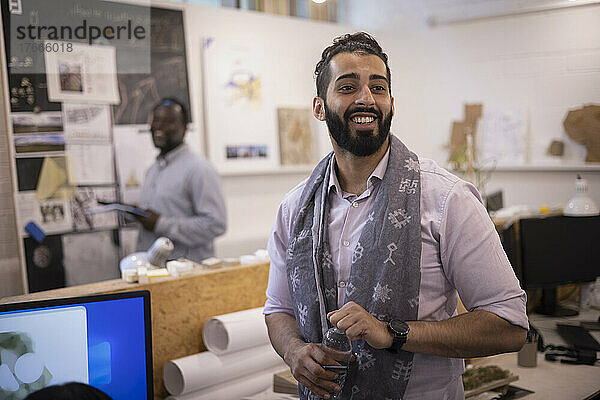 Lächelnder junger Geschäftsmann mit Schal steht im Büro