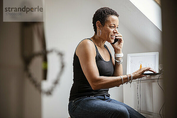 Reife Frau telefoniert im Heimbüro mit dem Smartphone